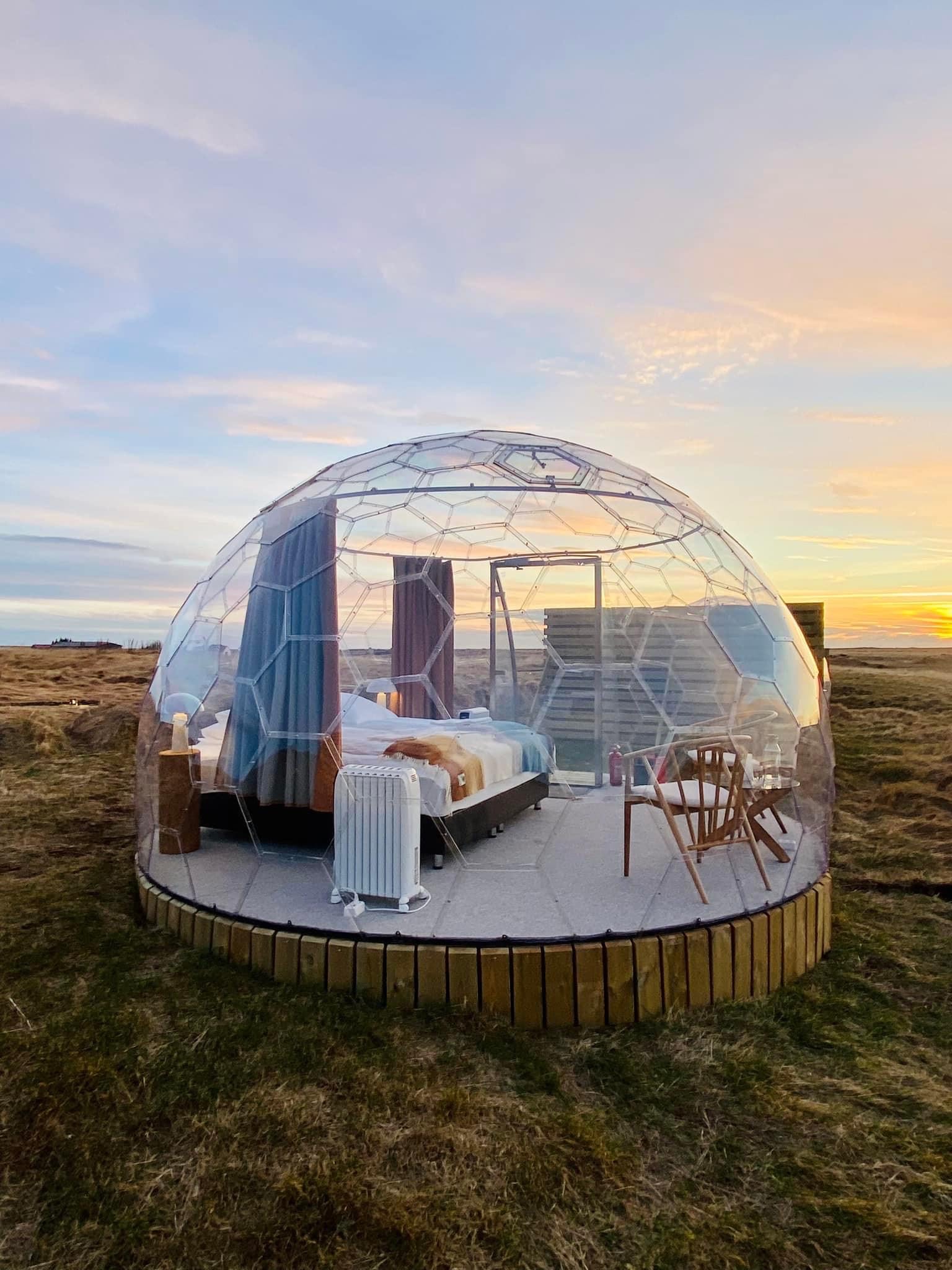 Glamping igloo dome glowing at night under the northern lights in Iceland