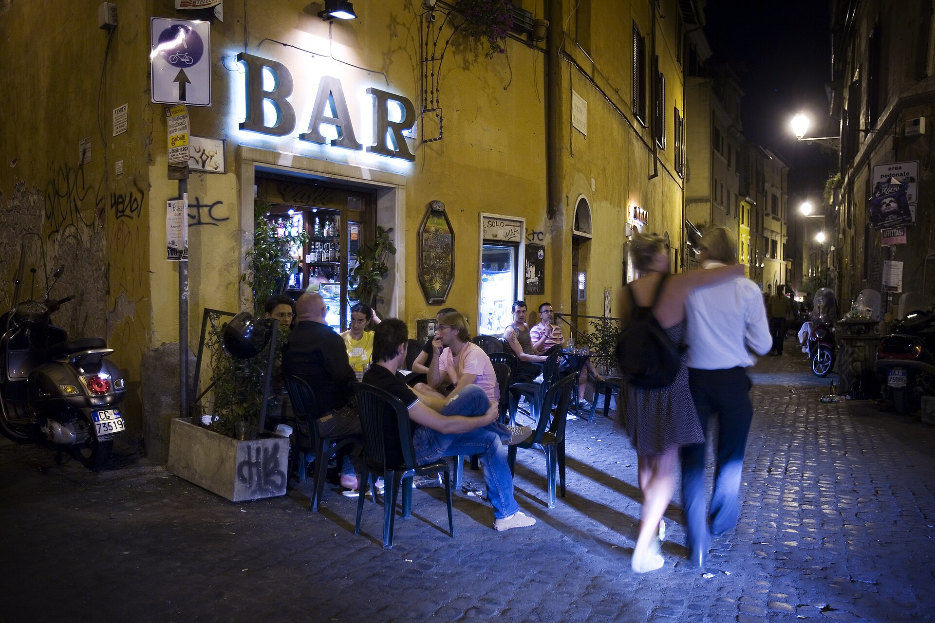 A narrow cobblestone street lined with trattorias in Rome's Trastevere neighborhood at night